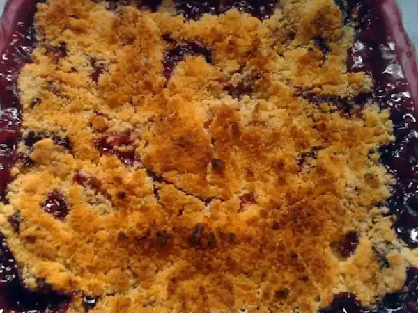 Delicioso crumble de ciruelas recién horneado, con una capa dorada y crujiente sobre la fruta jugosa.