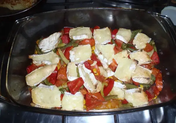 Zapiekanka z warzywami i kawałkami sera camembert w szklanym naczyniu.