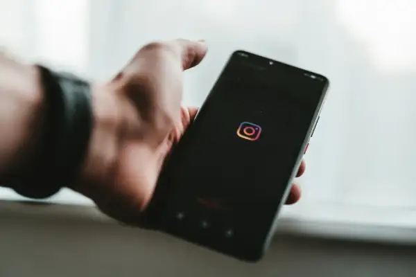 Dłoń trzyma smartfon z ikoną Instagrama. Dowiedz się, jak znaleźć zarchiwizowane posty na Instagramie, aby odzyskać stare wspomnienia.