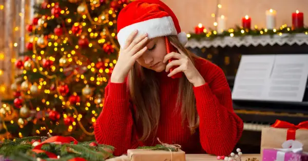 Smutna dziewczyna w czapce Mikołaja rozmawia przez telefon w Wigilię. W tle choinka i świece.