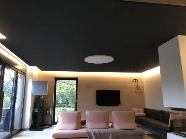 Nowoczesny salon z czarnym sufitem napinanym. Widać subtelne wady w postaci delikatnych zagnieceń na jego powierzchni.