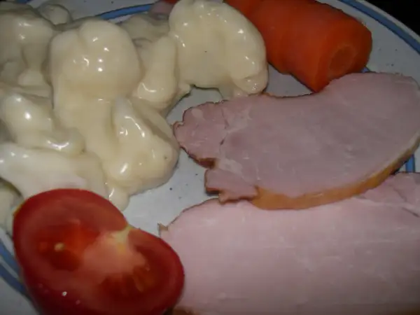 En tallrik med stuvad blomkål, skinka, en morot och en tomatklyfta. En klassisk svensk husmansrätt.