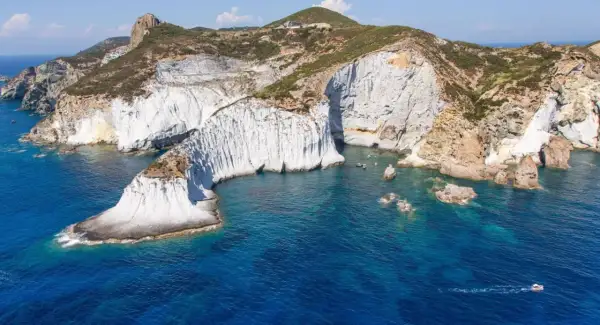 Scogliere bianche a picco sul mare blu intenso di Ponza. Un piccolo gozzo solca le acque cristalline, mentre la natura scolpisce la costa.