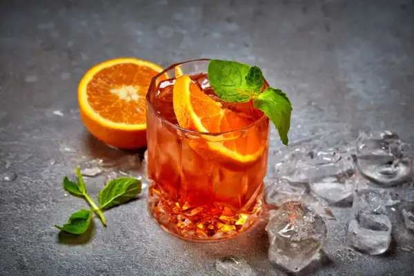 Un cocktail aranciato con fette d'arancia e menta, circondato da cubetti di ghiaccio per cocktail che non si scioglie, su uno sfondo grigio.