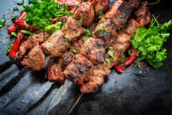 Soczysty kebab gruziński na metalowych szpikulcach, ozdobiony świeżą natką pietruszki i papryką.