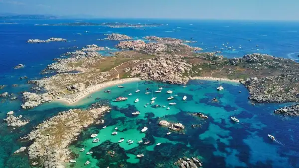 Vue aérienne d'une **excursion île Lavezzi** : eaux turquoise, plages de sable fin, rochers granitiques et nombreux bateaux au mouillage.