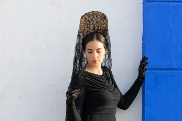 Mujer con peineta y mantilla negra, guantes de encaje, lista para una ocasión especial.