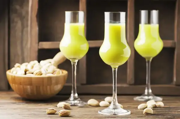 Zielony likier pistacjowy w kieliszkach, obok miseczki z pistacjami. Idealny przepis, jak zrobić wódkę ze spirytusu, by uzyskać taki smak.