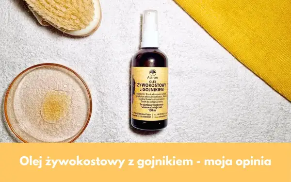 Olej żywokostowy z gojnikiem w buteleczce z atomizerem, obok kieliszka z płynem i szczotki do masażu. Naturalna pielęgnacja.