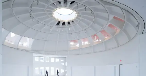 The expansive, white interior of the Faena Art Project Room features a striking domed ceiling with a central skylight. Two figures walk through the minimalist space.