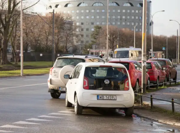 Biały Volkswagen up! i inne samochody stojące na jezdni, częściowo zasłaniające przejście dla pieszych.
