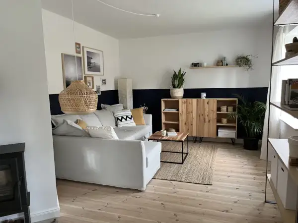 Salon moderne avec canapé gris, meuble en bois et tapis en jute. Le mur est peint en deux tons, blanc et bleu nuit, rappelant des techniques de peinture acrylique.