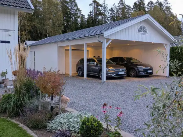 Vitt garage med två bilar under taket. En katt smyger i rabatten framför. Perfekt för att bygga garageport.