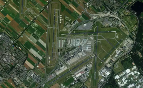 Widok z lotu ptaka na lotnisko Schiphol w Amsterdamie, otoczone polami i drogami.