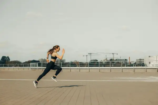 Kobieta w sportowym stroju biegnie, pokonując dystans 5 km. W tle widać miejską panoramę z dźwigami budowlanymi.