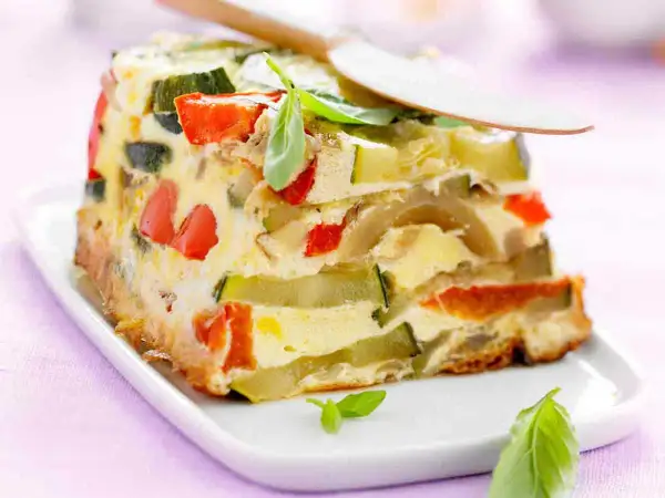 Tranche de terrine de légumes colorée, avec courgettes, poivrons rouges et une touche de basilic frais.