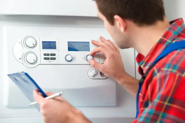 Tecnico regola la temperatura acqua sanitaria su una caldaia, con appunti in mano.