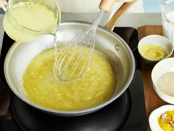 Flüssigkeit wird in eine Pfanne mit einem Schneebesen gegossen, um eine cremige vegane Hollandaise zuzubereiten.