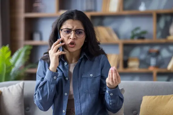 Donna con occhiali parla al telefono con espressione frustrata, un gesto della mano che suggerisce il desiderio di chiudere il telefono in faccia psicologia.