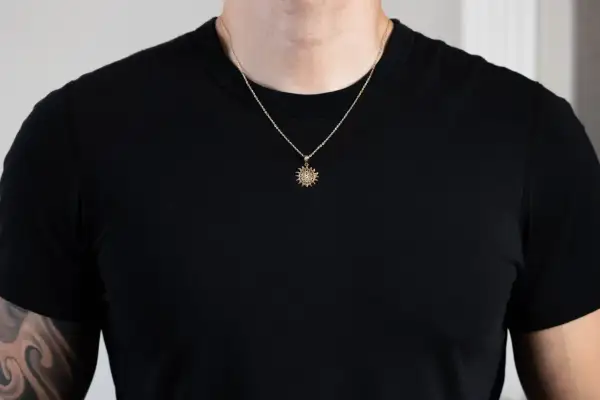 Un hombre luce un colgante sol oro con detalles intrincados sobre una camiseta negra.
