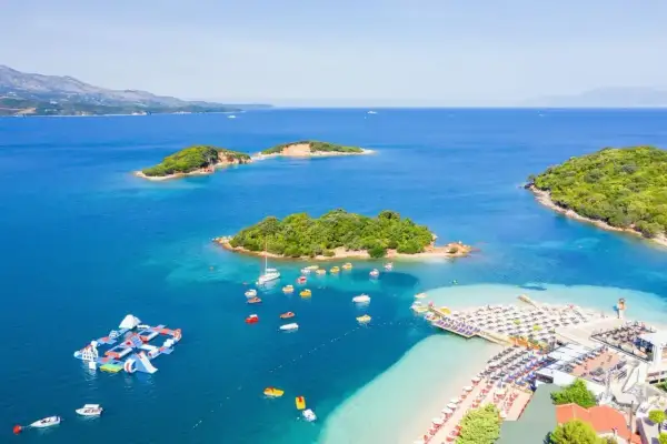Rajska plaża i wysepki na lazurowym morzu w Albanii. Wodne atrakcje, łodzie i leżaki zapraszają do wypoczynku.