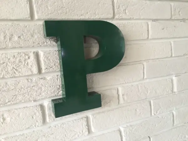Une lettre murale verte en forme de P est fixée sur un mur de briques blanches.