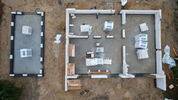 Budowa domu z bloczków betonowych. Materiały budowlane leżą na płycie fundamentowej, czekając na montaż ścian, by zapewnić niski współczynnik przenikania ciepła.