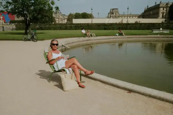Une femme lit au soleil, profitant d'un moment de détente pour ou bronzer à Paris, près d'un bassin.
