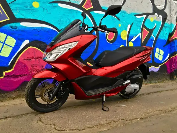 Czerwony skuter Honda PCX 125 na tle kolorowego graffiti. Mimo że jest to niezawodny model, warto pamiętać o jego awaryjności w ekstremalnych warunkach.