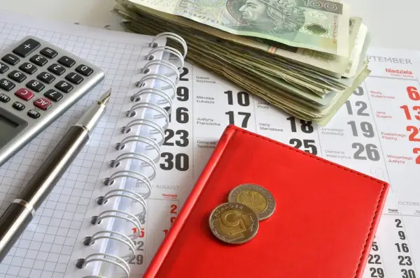 Kalkulator, długopis, stos banknotów i monety na kalendarzu. Przygotowanie do zapłaty opłaty od pozwu w postępowaniu upominawczym.
