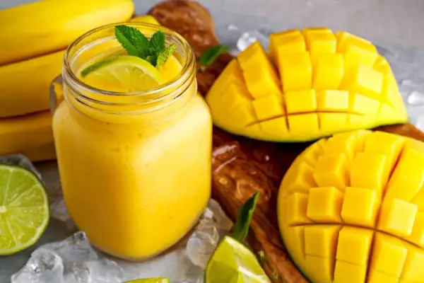 Orzeźwiający koktajl z mango, udekorowany miętą i limonką, obok pokrojonych owoców i bananów.
