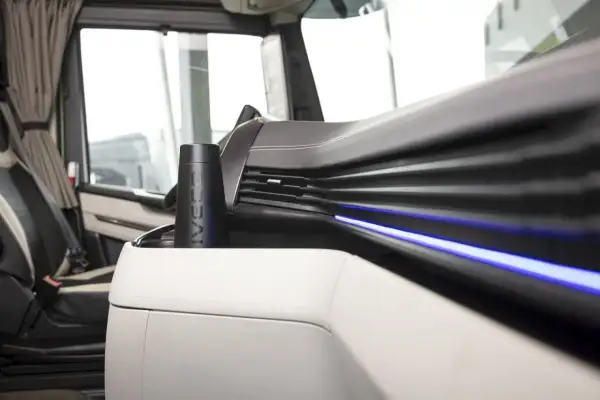 Un porte-gobelet noir avec le logo IVECO, un des indispensables du routier, est placé sur la console centrale d'un camion.