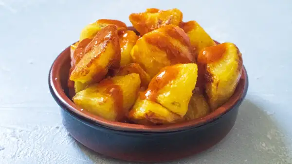 Knusprige Kartoffelstücke, überzogen mit einer würzigen Sauce, serviert als köstliche Patatas Bravas in einer rustikalen Schale.