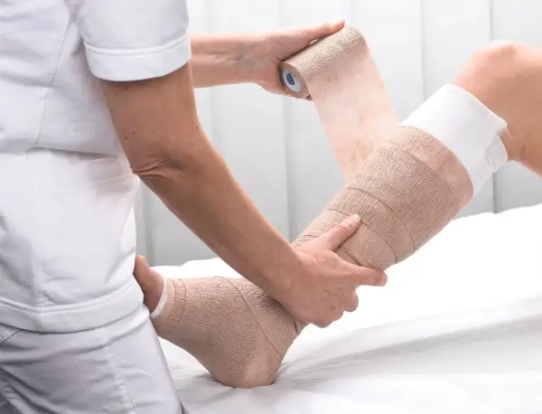 Fachkraft übt Kompressionsverband Techniken an einem Bein aus. Der Verband stützt und stabilisiert.