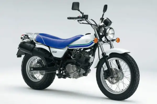 Biały motocykl Suzuki Van Van z niebieskim siedzeniem i zielono-niebieskimi pasami na baku. Idealny na miejskie wyprawy.
