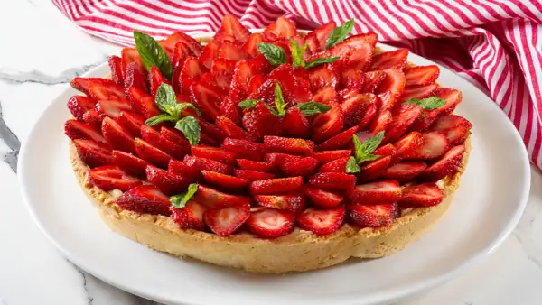 Deliziosa crostata alla crema, ricoperta da fragole fresche affettate e guarnita con foglie di menta.