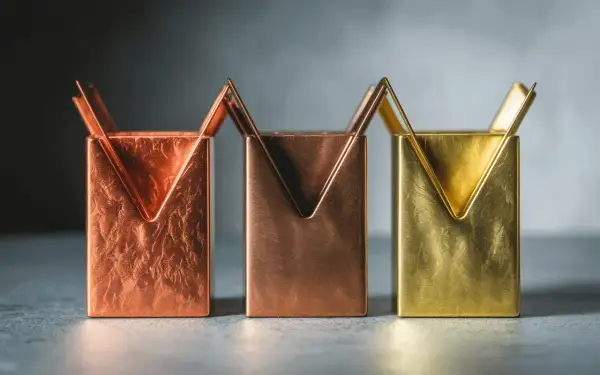 Trois porte-stylos aux formes géométriques, en laiton et cuivre, aux textures variées.