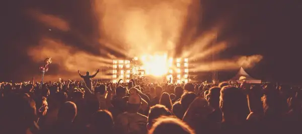 Tłum ludzi na Sunrise Festival Poland, z rękami w górze, w blasku świateł scenicznych i dymu.