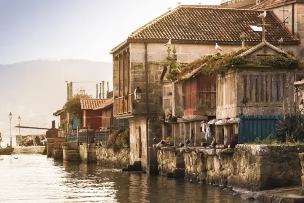 Casas de piedra y madera junto al agua, gaviotas en los tejados. Un ejemplo de los pueblos bonitos de Galicia.
