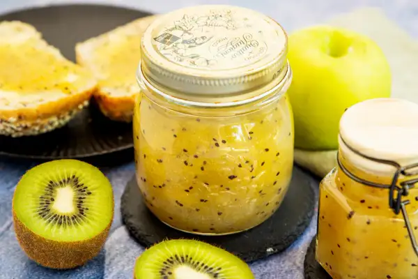 Ein Glas hausgemachte Kiwi-Marmelade mit frischen Kiwis und Toast.