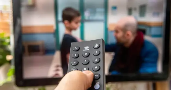 Dłoń trzymająca pilot do telewizora, na ekranie widać scenę z dzieckiem i mężczyzną. Czas na ulubiony serial, opłacony abonament radiowo-telewizyjny działa!