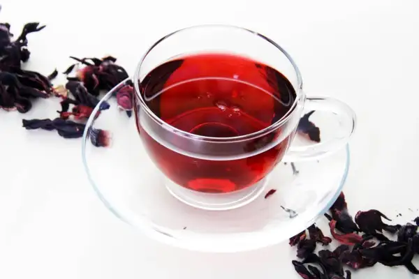 Szklana filiżanka z czerwonym naparem, obok suszone płatki hibiskusa. Idealny napój na odchudzanie.