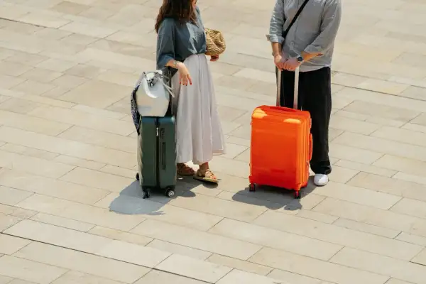 Para podróżnych z bagażami, w tym zielona podręczna walizka na kółkach Wizzair, gotowa na wakacje.
