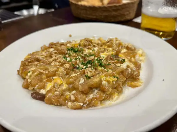 Delicioso revuelto de bacalao con trocitos de frutos secos y perejil picado, servido en un plato blanco.