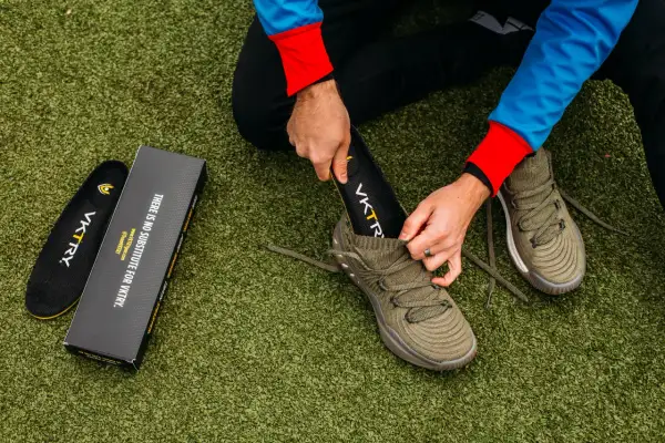 Un homme change la semelle intérieure de sa chaussure de sport sur un terrain artificiel.