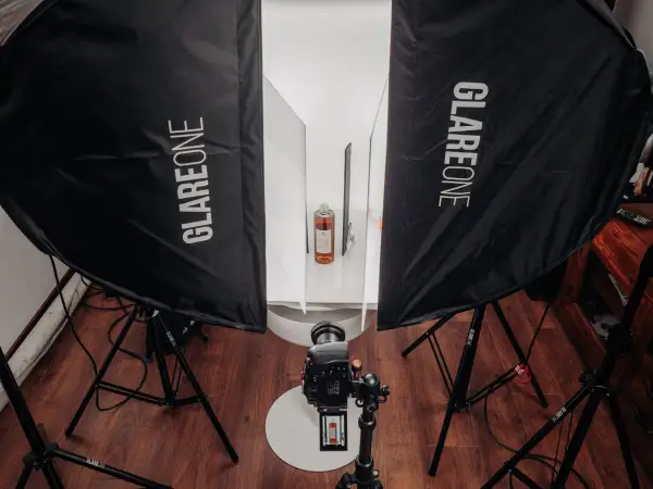 Profesjonalna fotografia produktowa jak zacząć? Zestaw oświetleniowy z dwiema lampami Glareone, aparatem i butelką w tle.
