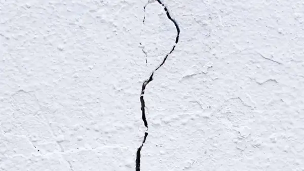 Una pared blanca con textura rugosa muestra grietas por dilatación, una línea oscura que se abre paso a través de la superficie.
