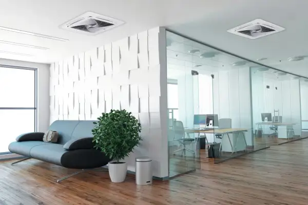 Un moderno ufficio con un divano, una pianta e un condizionatore incassato nel controsoffitto. La zona lavoro è separata da pareti in vetro.