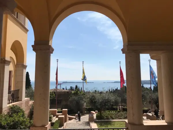 Arco con vista sul lago, giardini e bandiere che sventolano, ricordando l'atmosfera della villa d'Annunzio.