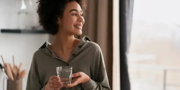 Une femme souriante tient un verre d'eau, un geste simple qui symbolise le luxe de l'eau de riche, une hydratation pure et précieuse.